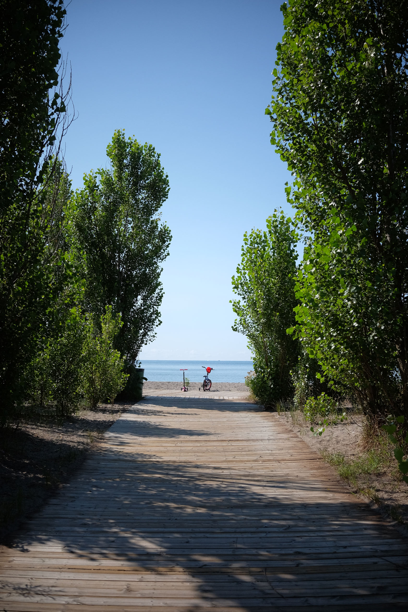 looking down a boardwalk in bright daylight towards an ocean.