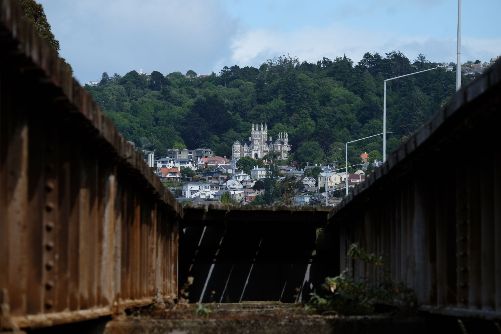 image between two steel beams looking up to a castle keep like building jutting out from a green hillside.