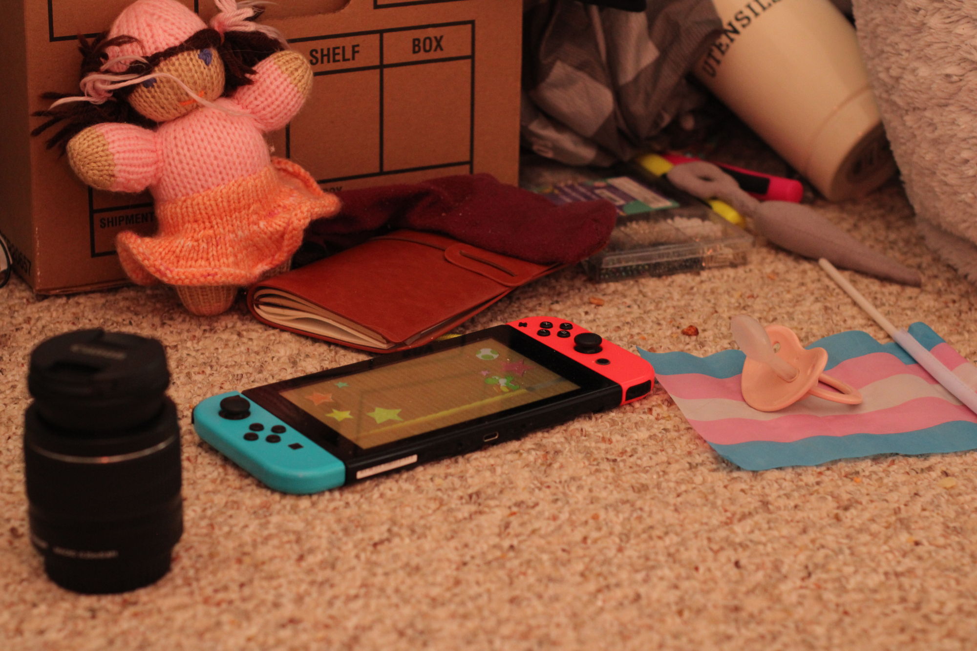 still life photo of game console with cute character on it, pink pacifier, and a medium length camera lens and a dolly.