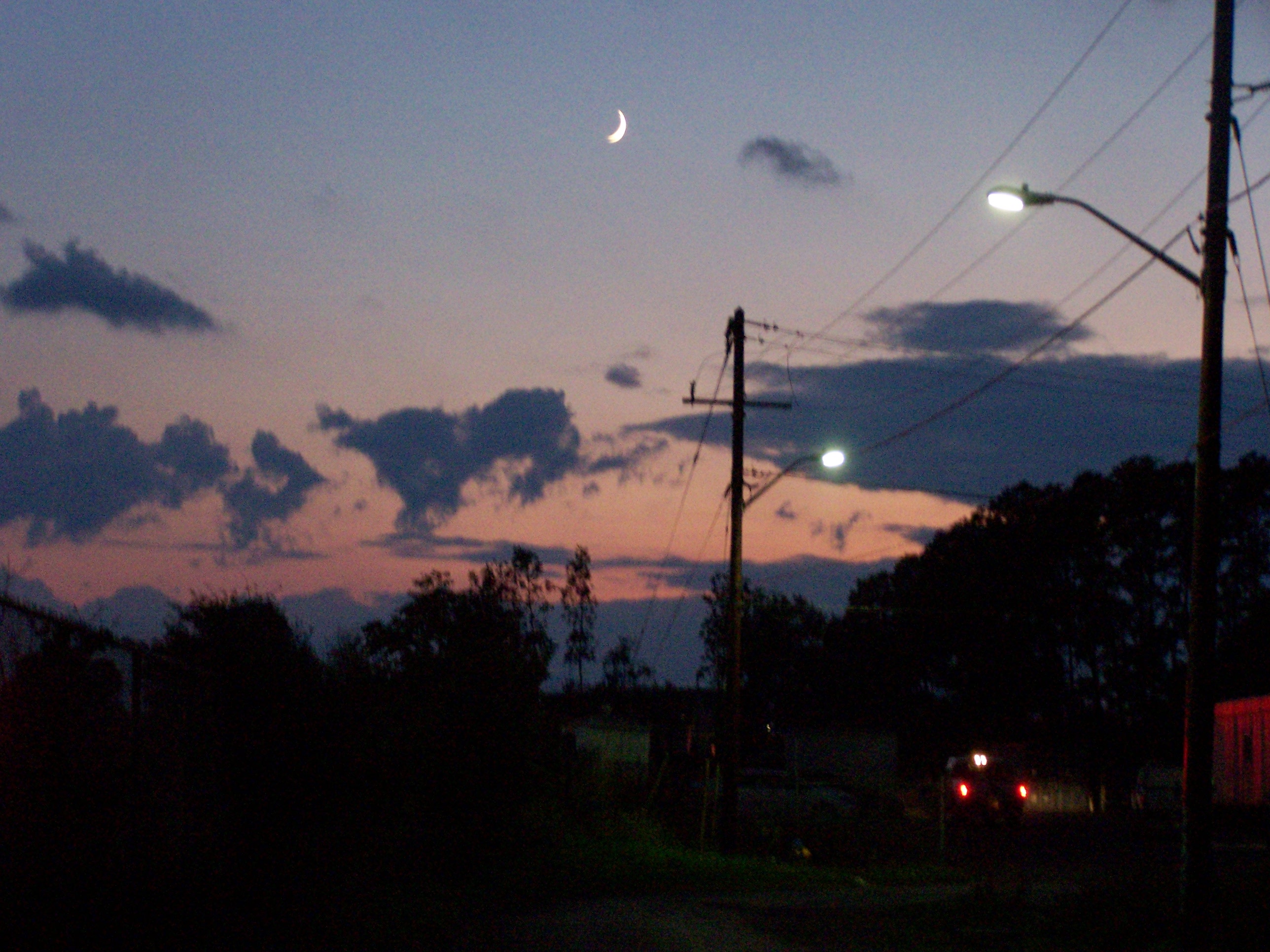 transition to a nightime. the horizon is occupied by a thin band of orange and purple at the bottom, and the rest is filled with an increasinly dark gradient of blue and grey. towards the bottom of the horizon is interesting cloud shapes that follow the cut off of orange, and the centrepiece of the image is a bright white crescent moon.