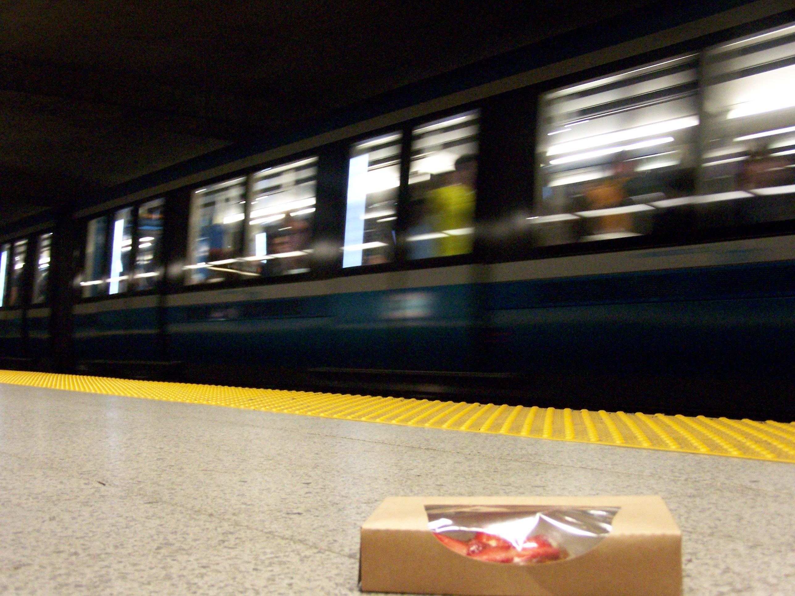 underground metro station from a low angle. the train is moving out of the station, and there is a box of strawberries on the platform.