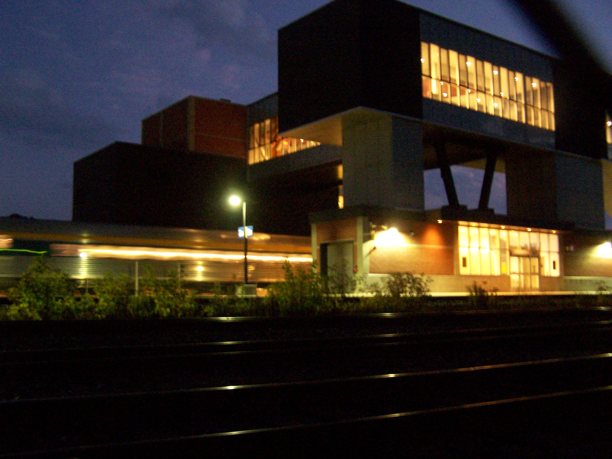 train station in the night. there is a train passing through, and the streak of soft, orange interior lighting calmly illuminating the outside. the train station also uses calm orange lights.