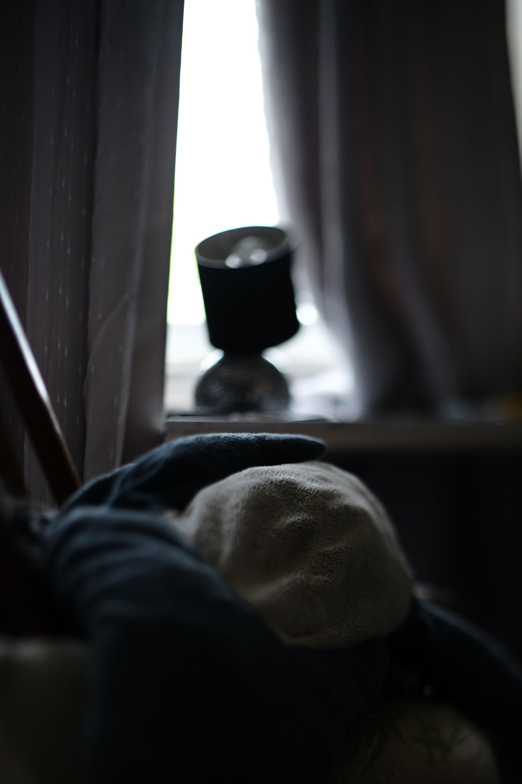 dark indoor photo with very little in focus of a shark plush laying upside down towards a window with two curtains framing it. the outside is glowing white, and the curtains are pitch black.