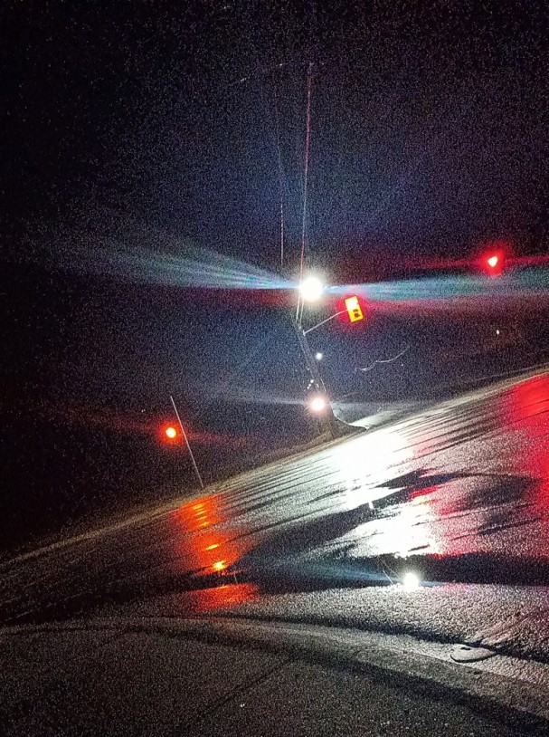 dramatically tilted camera on a subruban arterial signalled intersection. it is night time, and the illumination of the street lights is reflecting off the wet road surface.