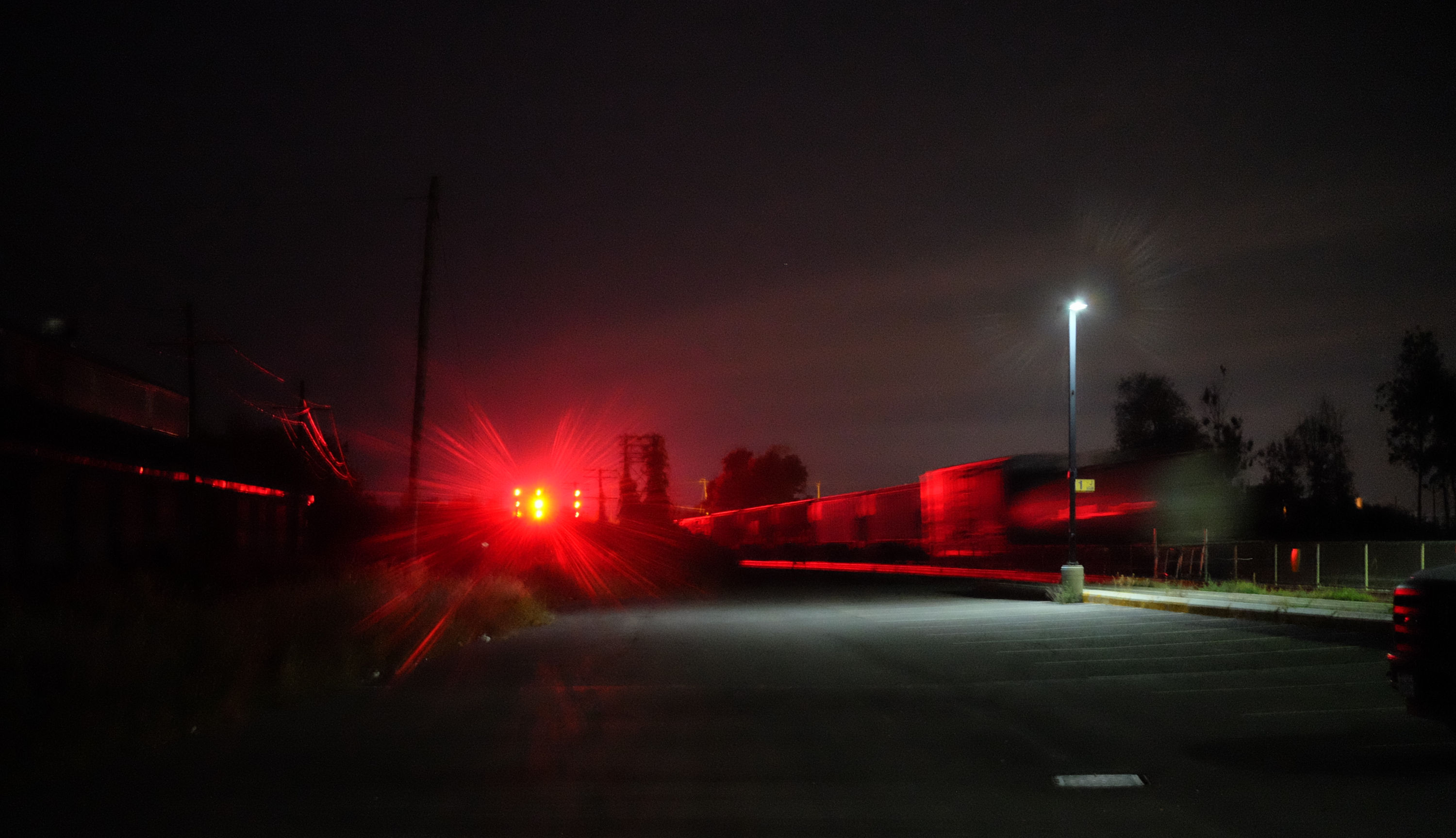 night photograph of a train barrelling towards a bright red light, indistinguishable due to flare. the train is also illuminated red by this light.