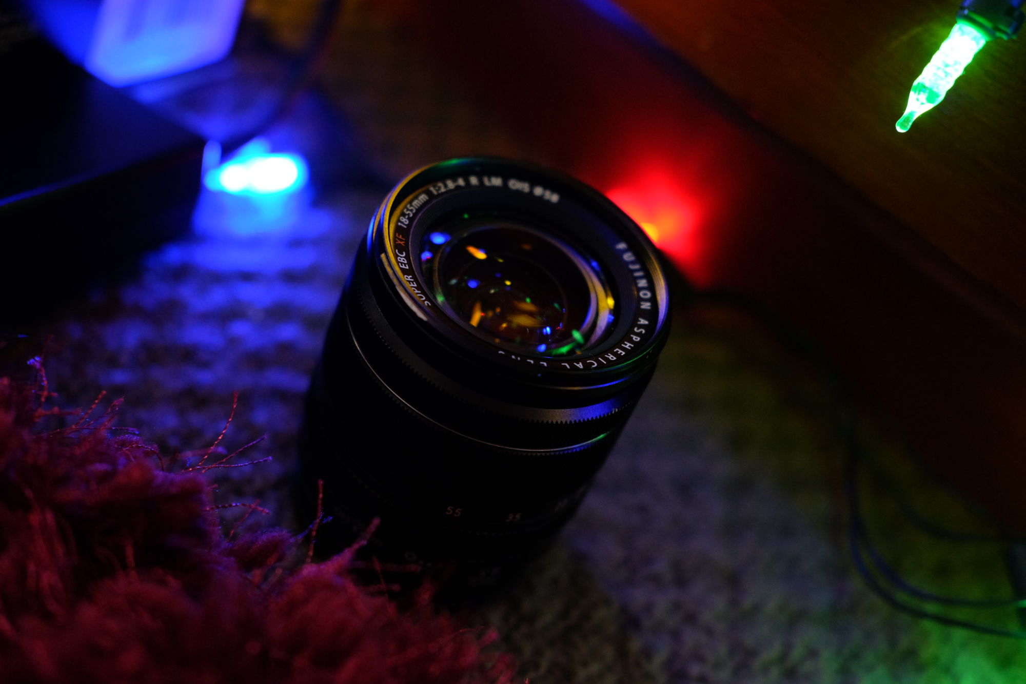photogaph of 18-55mm lens on ground at an angle. there is fairy lights reflecting in the front element.