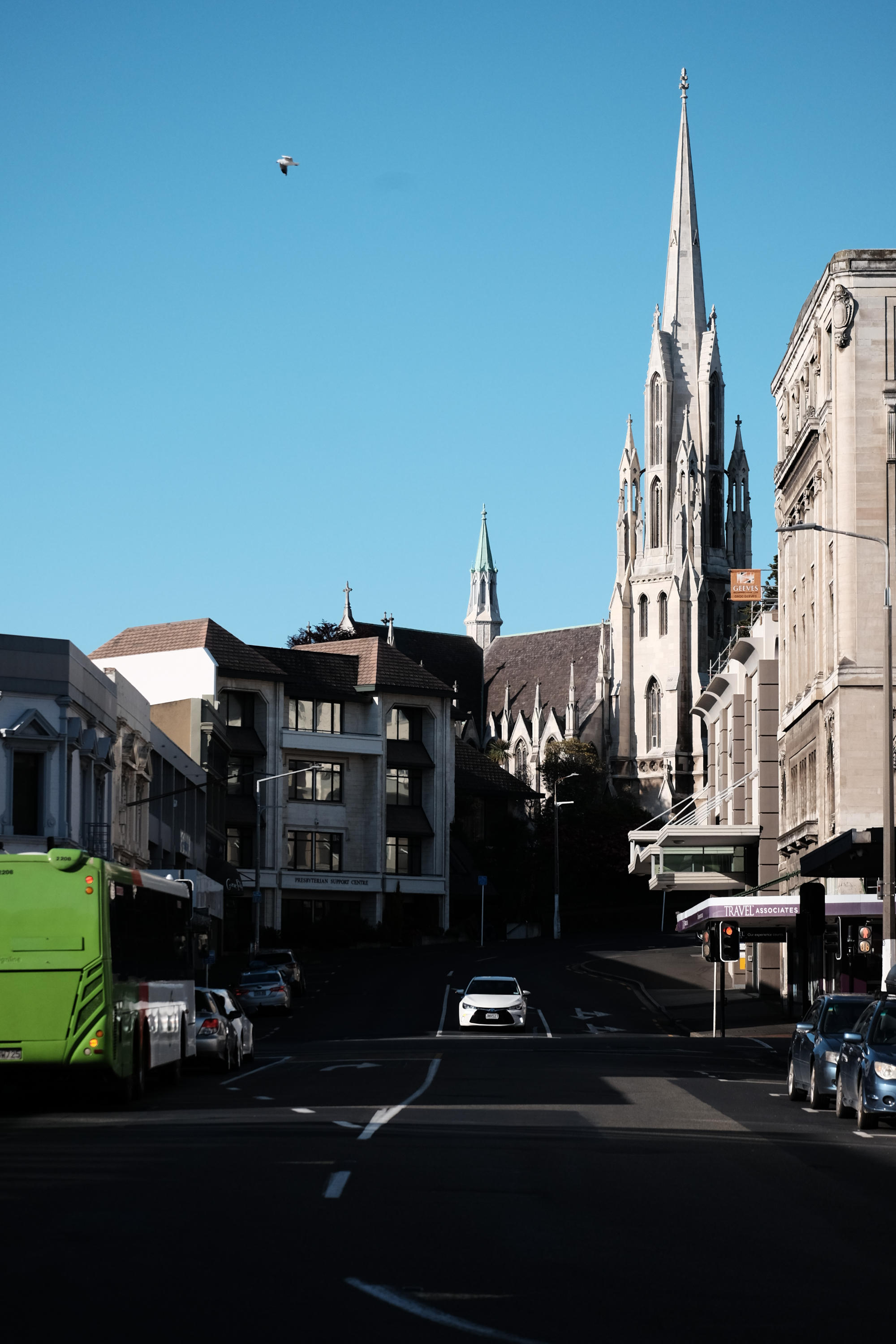 desaturated photo looking down a street with a church in the corner. there is a junction where a green bus is stopped, and the rest of the road is empty