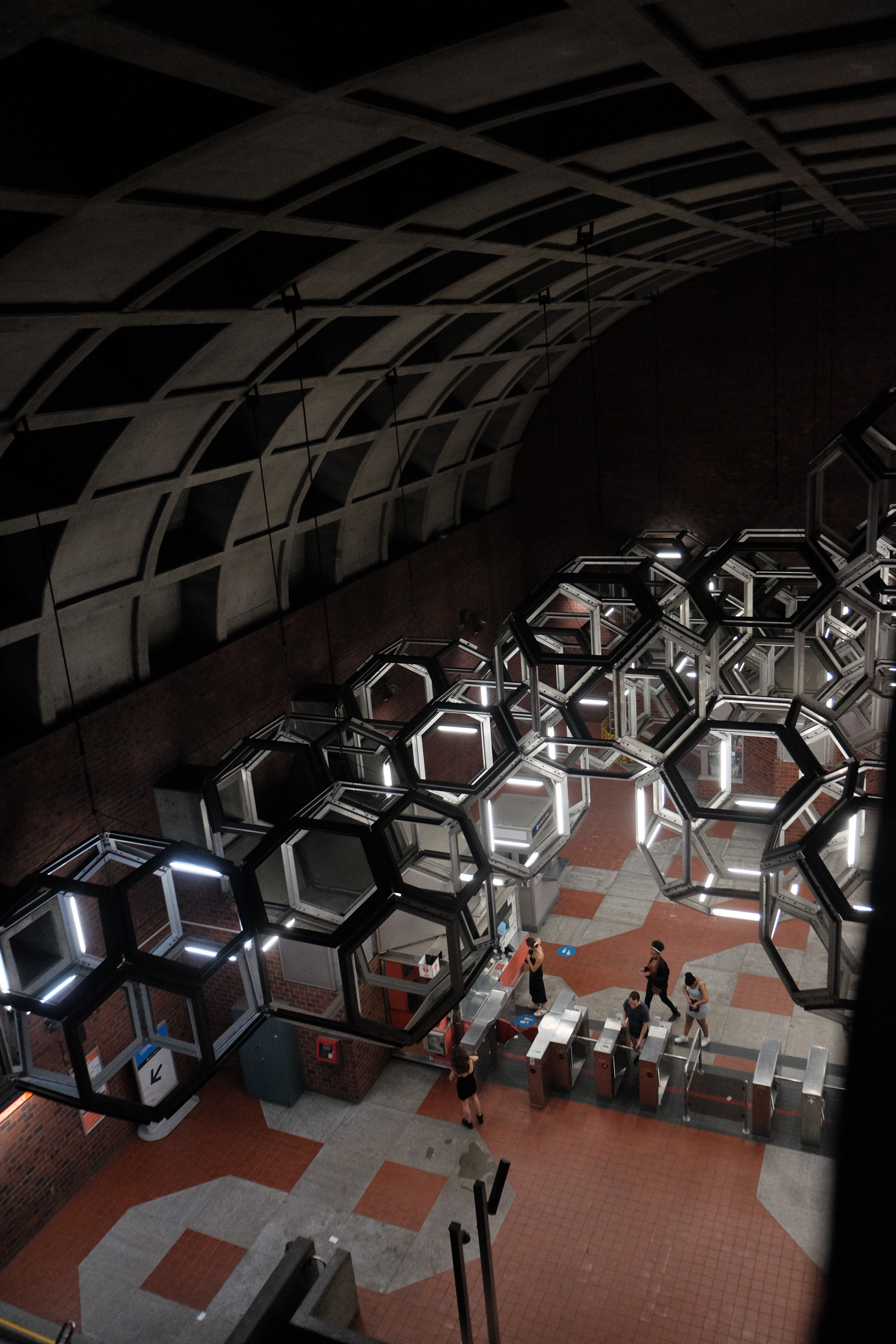 large dark underground structure with large hanging lighting fixtures that are 3 dimesnional and have hexagonal faces