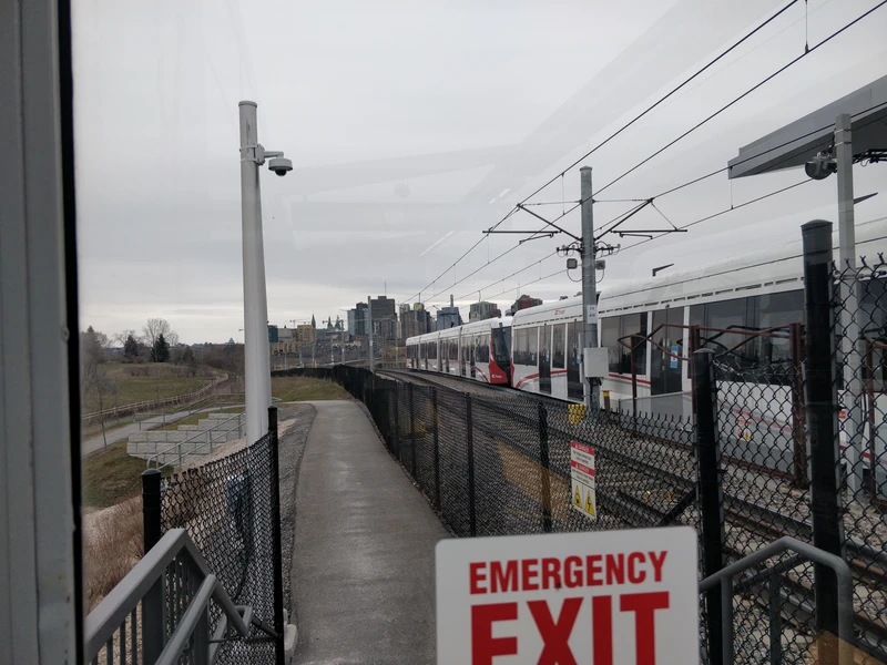 photograph of a citadis spirit tram coupled together with a second tram 
                from a field overlooking ottawa's cbd.