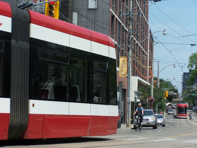 historic classic toronto brick architecture buildings accompanied by two red trams and one cyclist. only the cabs of the trams are visible, with one tram perpendicular to the camera, and another parallel.
