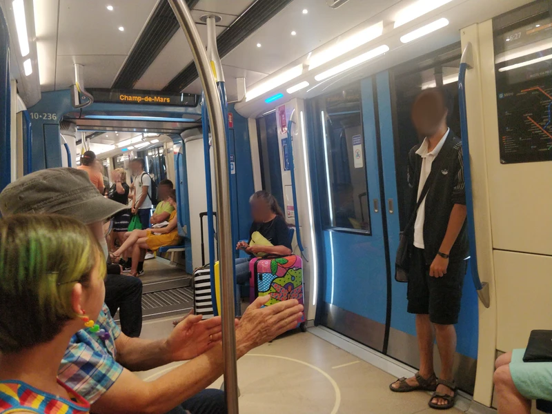 interior of a wide, colourful metro car. it is primarily white with blue accents, and colour changing lights there are various people sitting and standing near the closed doors and open gangways.