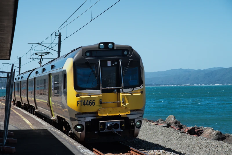 matangi train approaching a station in front of a bright blue bay.