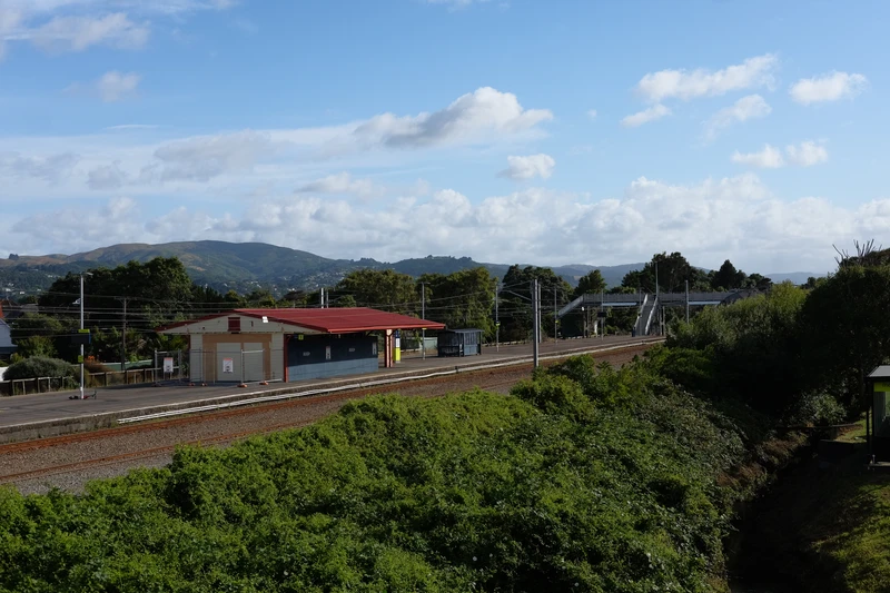 photograph of a small train station styled like a hut as a island platform. suburbs and hills are visible in the distance.