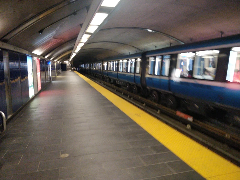 looking down the length of an underground metro station. the train on the opposite platform has it's large tyres visible.
