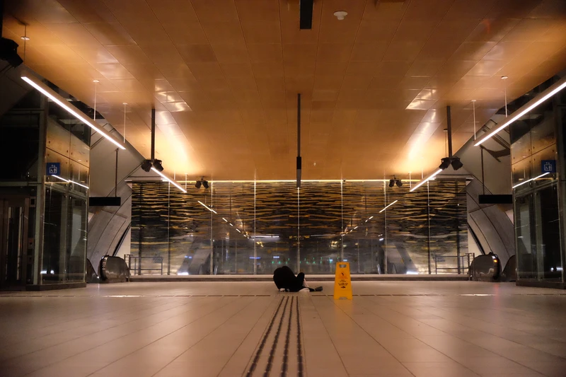 low to ground photo of metro station with yellow light and a dark ceiling featuring a next arrivals board.